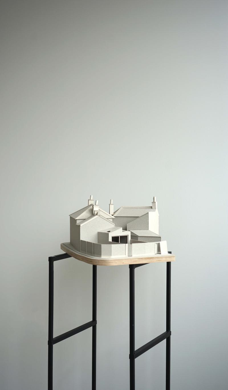 1:50 Building model of Woodbine Place. 

Grey board existing and proposed building model with a plywood base, sited on two steel plinths.